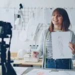 Smiling fashion designer presenting sketch in studio, being recorded on camera.