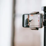 Apresentador gravando aula online com celular em tripé, guia de monetização de cursos online