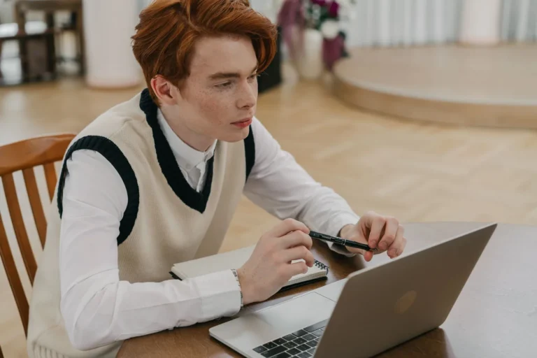 Jovem concentrado em aprendizado online em casa, usando laptop e caderno, representando melhores práticas EAD