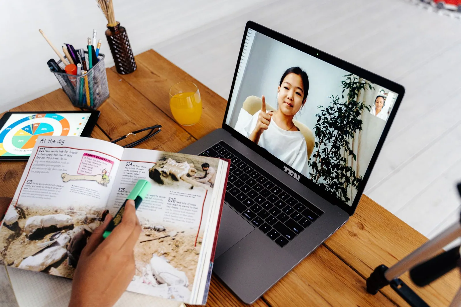 Mulher em tela de notebook durante sessão de ensino digital com materiais educativos ao lado
