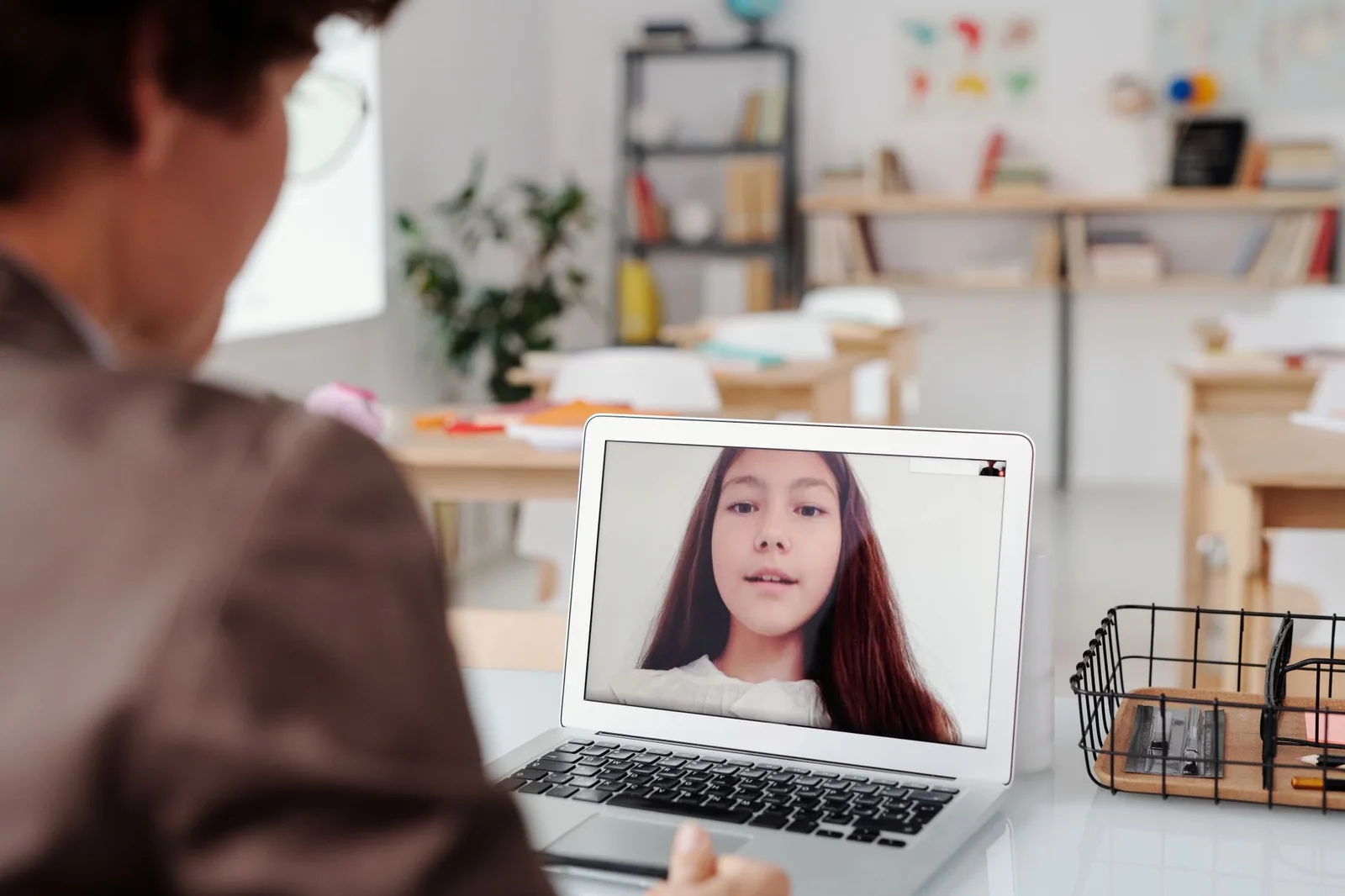 Professora utilizando laptop para aula virtual com aluna na tela, ilustrando metodologias de ensino online eficazes
